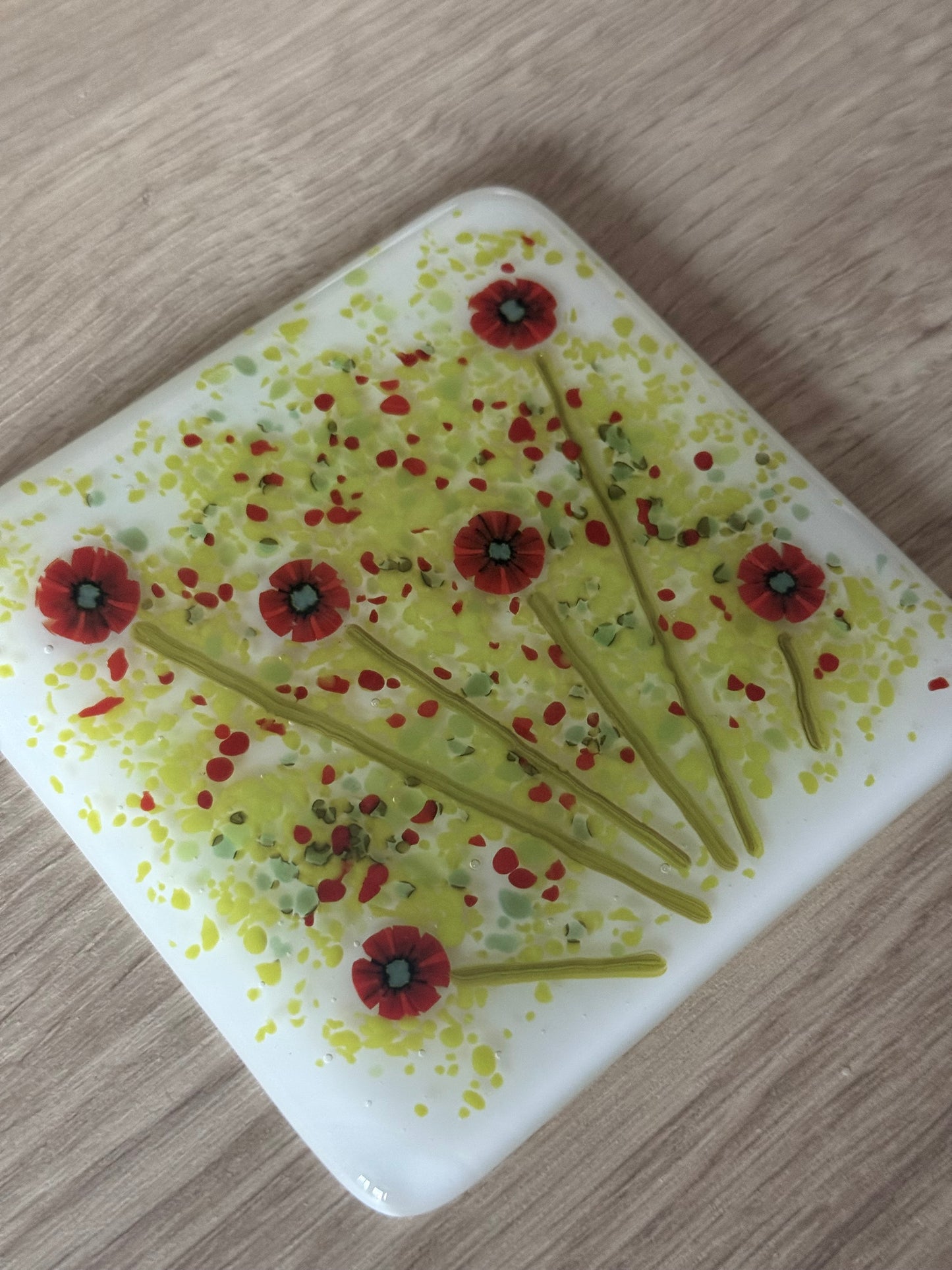 A square fused glass coaster with a white background and a floral poppy design in red and green.