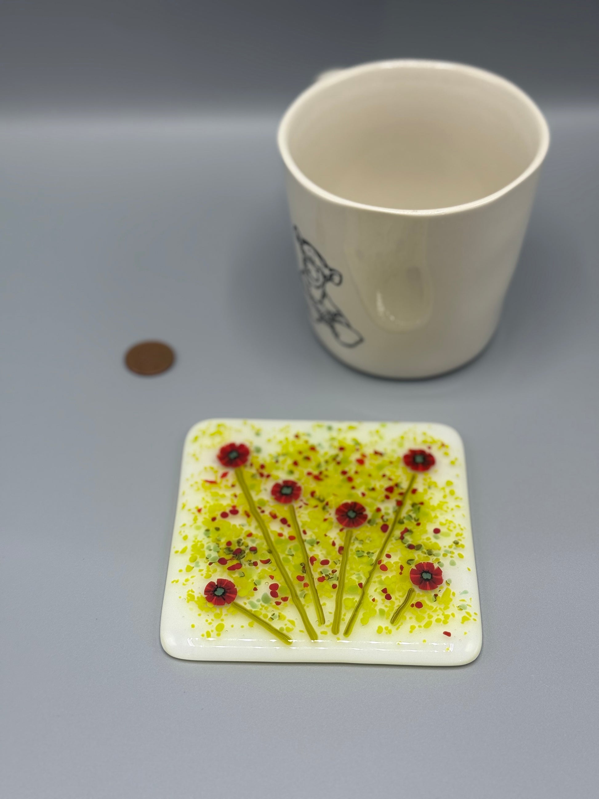 Coaster with floral design next to a cup and coin on a gray background